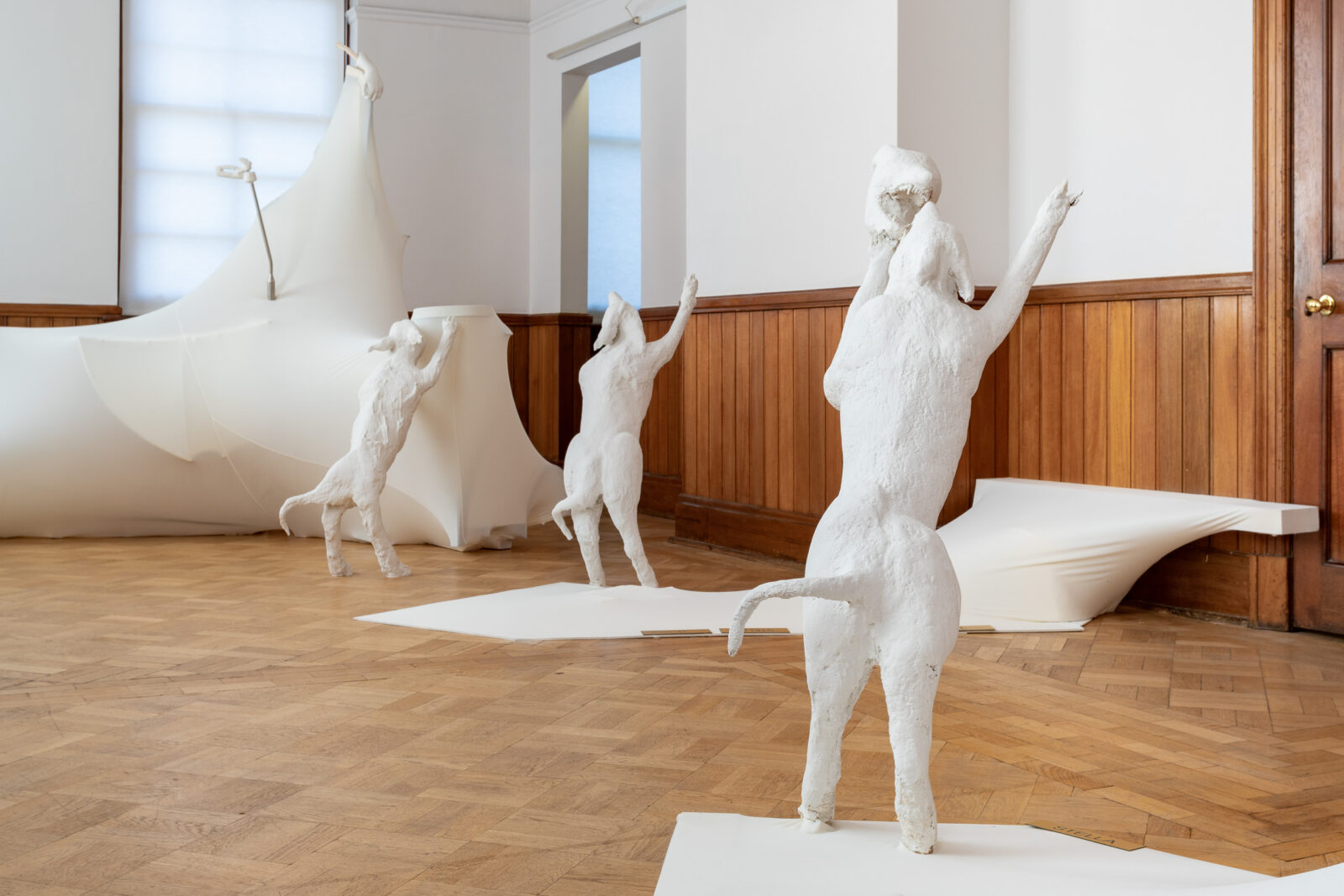 Three white sculptures of dogs in upright positions