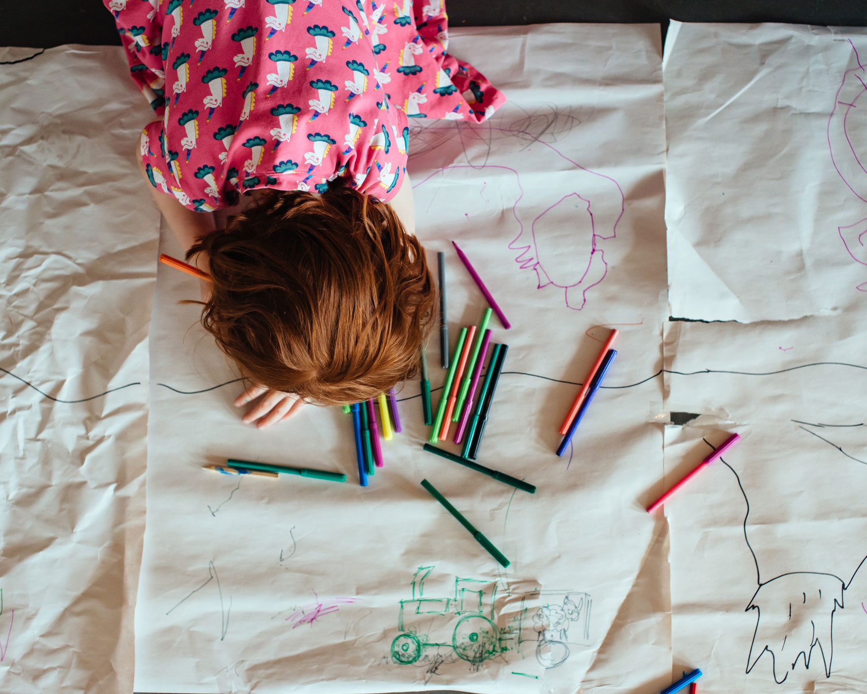 A child draws on large sheets of paper surrounded by coloured pens