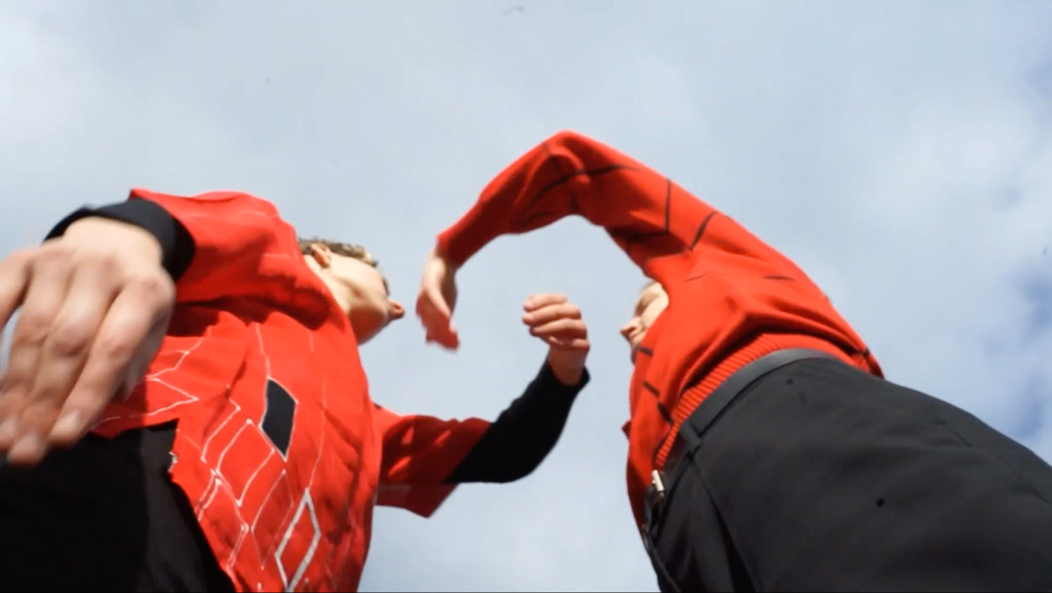 A still from Tora Hed's film Let it land, a photo from a low angle looking up at two dancing figures wearing red tops and navy trousers