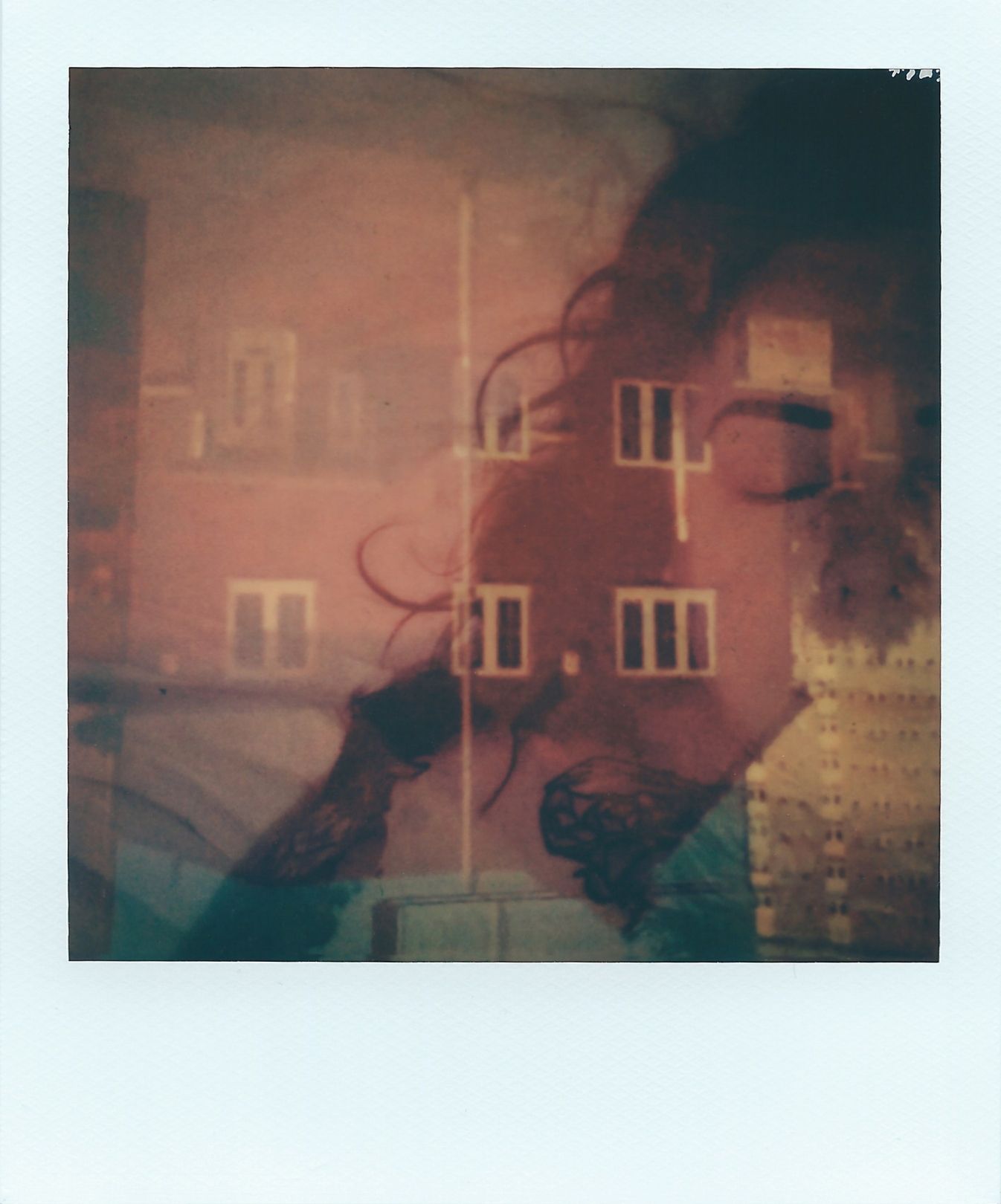 A polaroid image of the head and shoulders of the artist, with her eyes closed, overlaid with an upside-down image of a two storey house, high-rise flat and blue sky. Both layers are partially transparent, the colours are mostly pinks, purples and hints of blue.