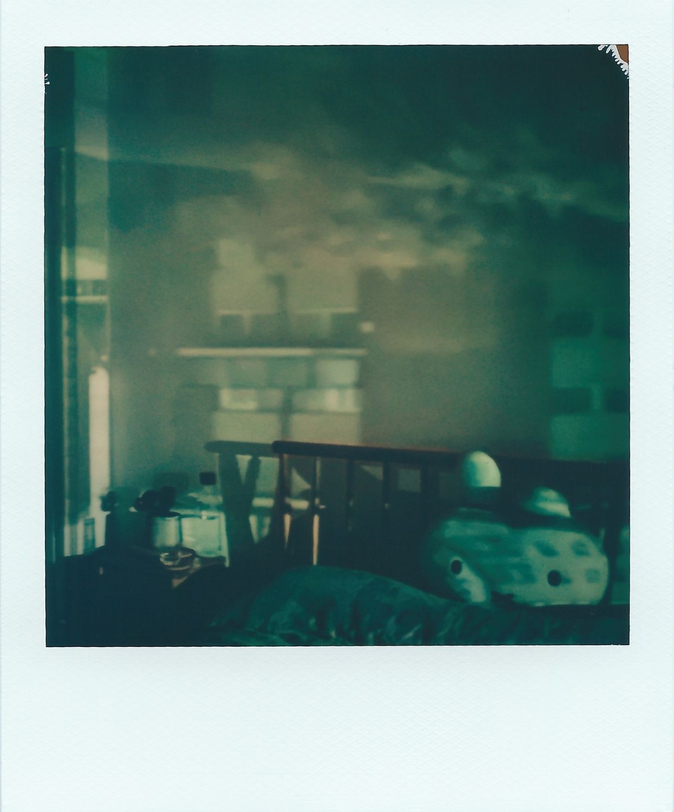 A polaroid image of four flat windows appear upside-down within a bedroom. The image covers one wall, and a murky blue sky overlaps the bed. The colours are mostly murky browns, green and blue.
