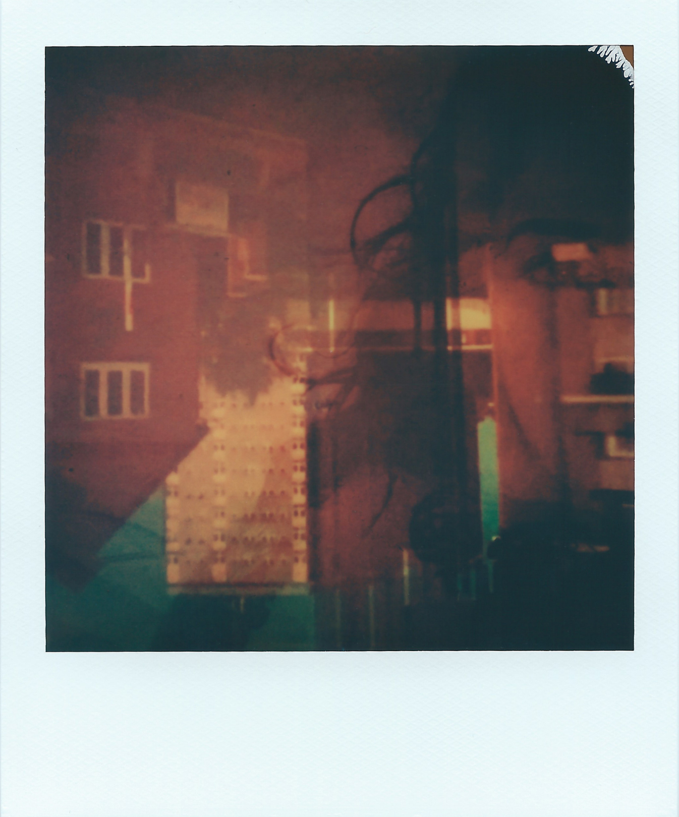 A polaroid image of one side of the artist’s head, with her eye open, overlaid with an upside-down image of a busy suburban street. Both layers are partially transparent, the colours are mostly burnt pinks, purples and hints of blue.