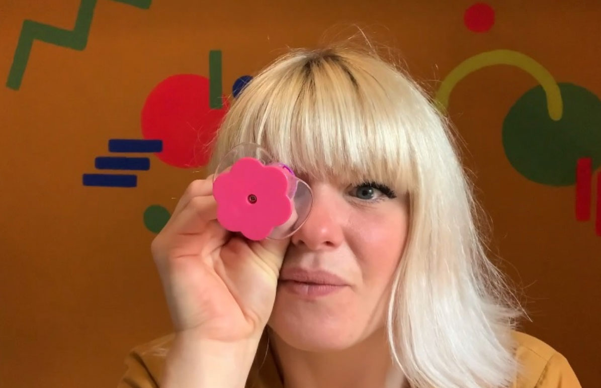 Stephanie Jefferies holds a pink plastic flower in front of her face with abstract shapes in the background