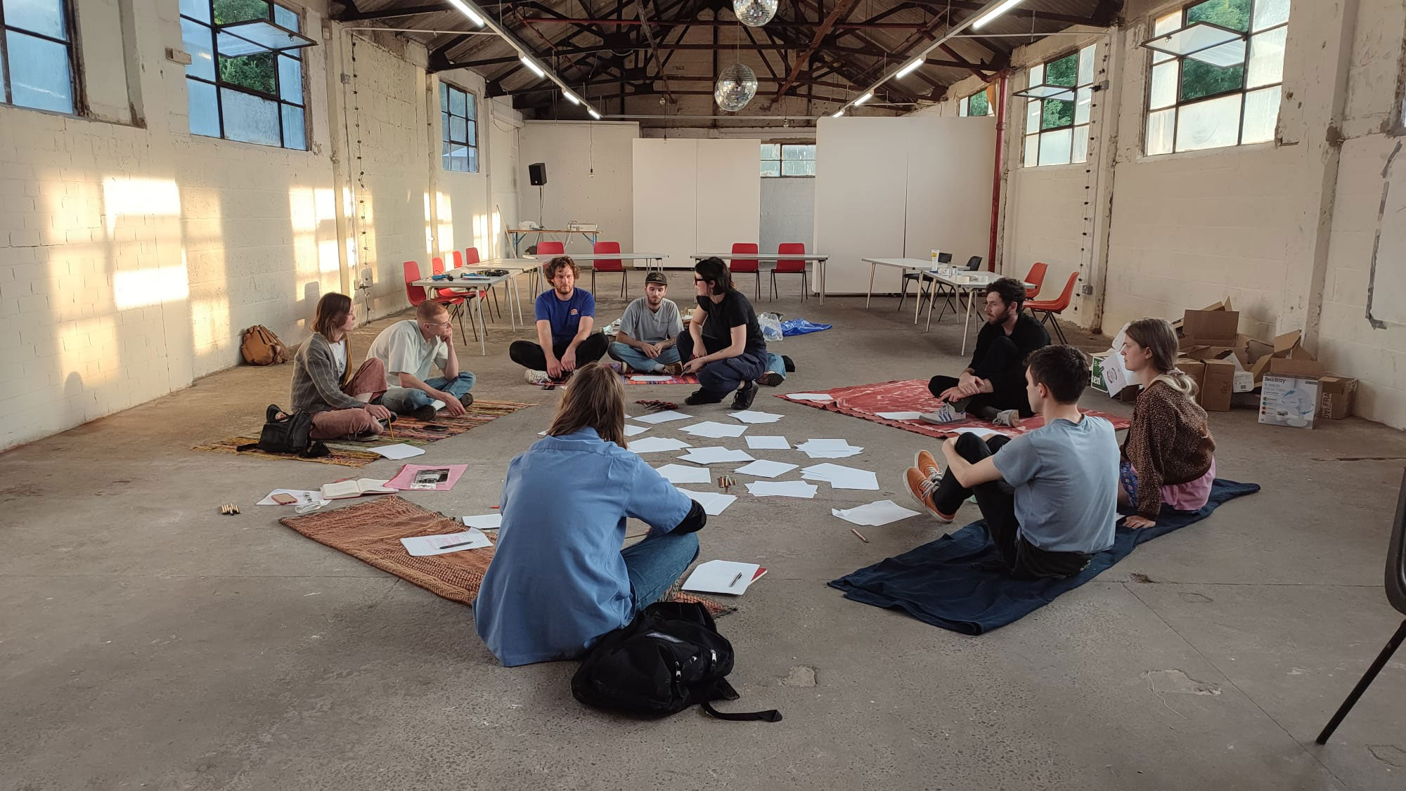 A group of people sat on the floor with white pieces of paper between them