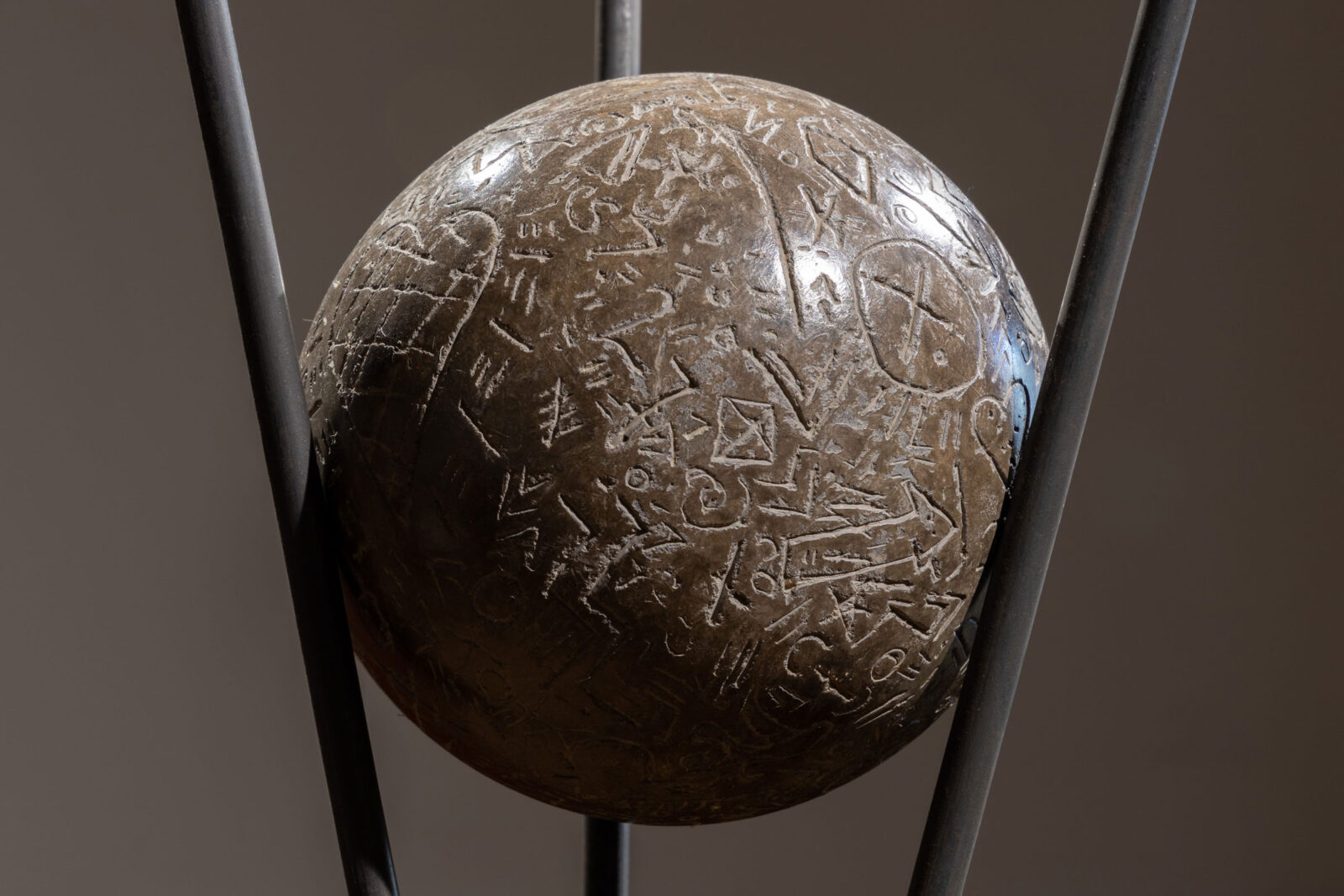 A polished sphere of clay in a tripod of metal rods, carved with symbols