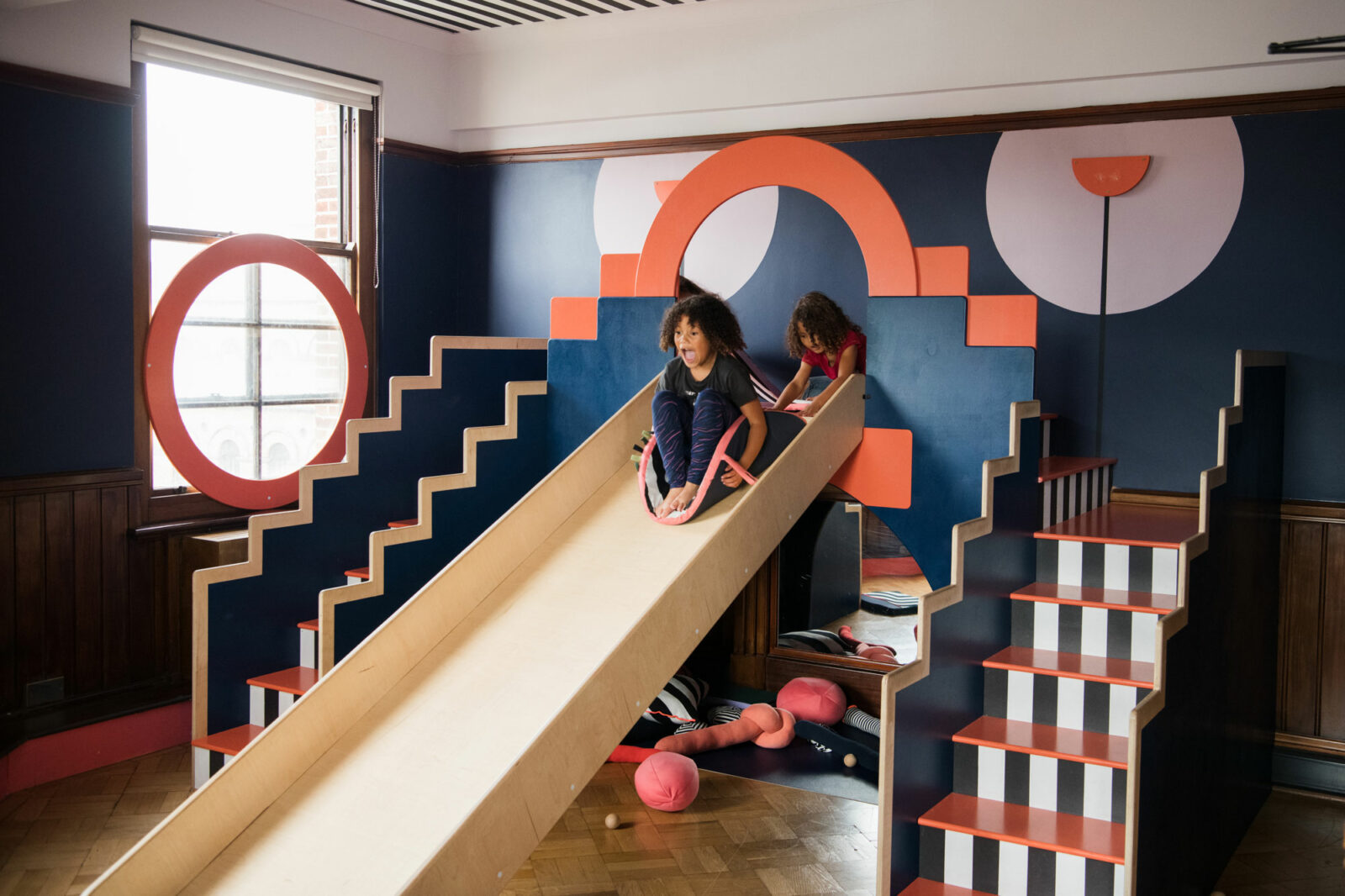 Two children whizz down the slide in The Tetley's free artist designed play space for under 5s