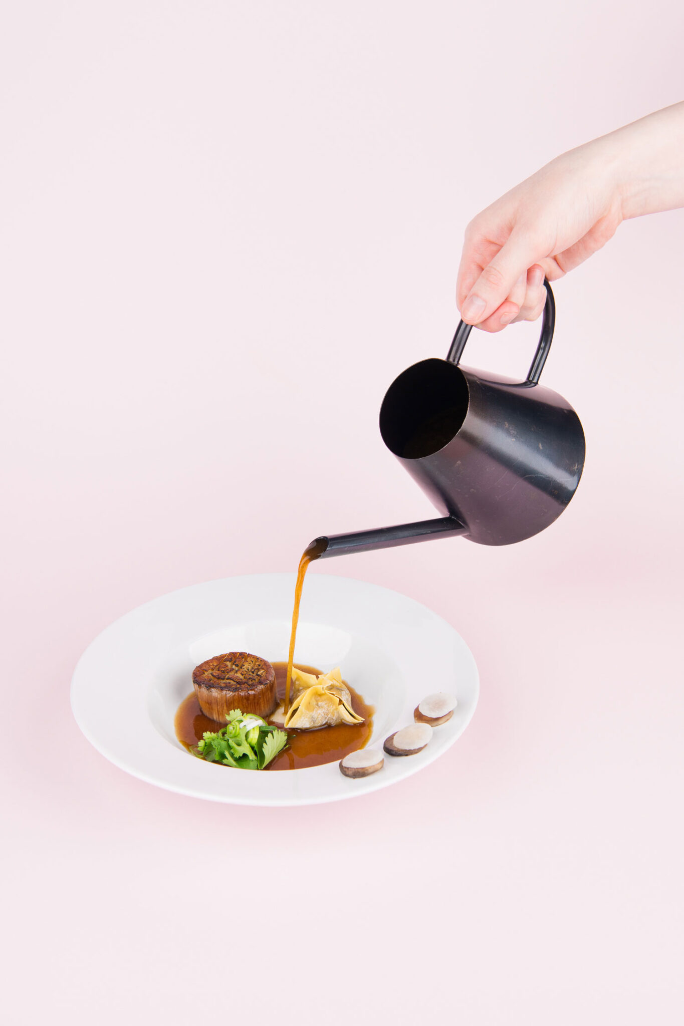 A black teapot pours a golden brown broth over a dumpling