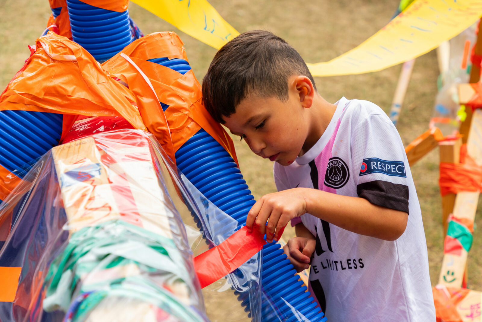 A child attaches bright tape to a brightly coloured structure in the park