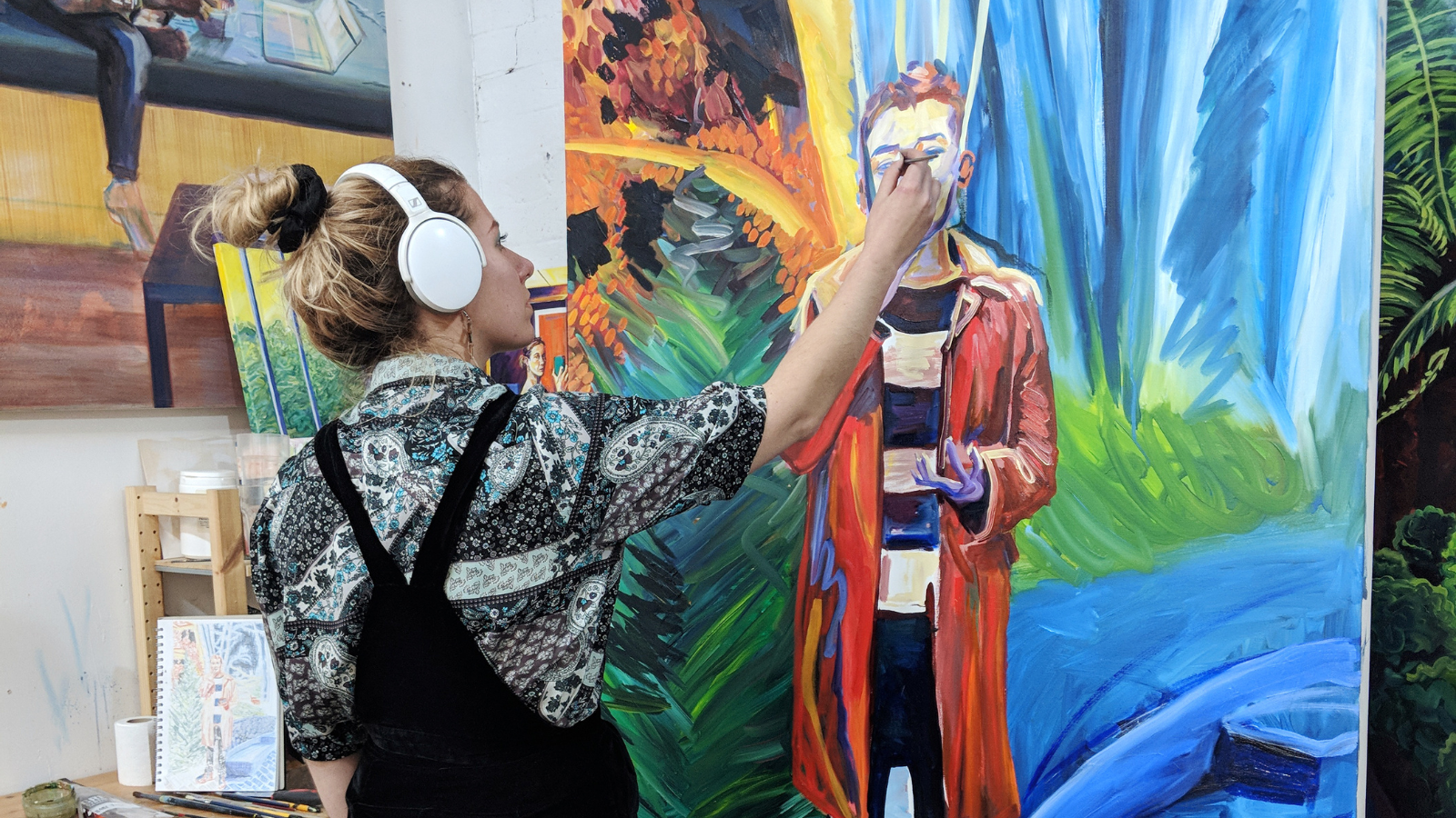 A photo of artist Julia working in her studio. She is painting a colourful oil painting portrait
