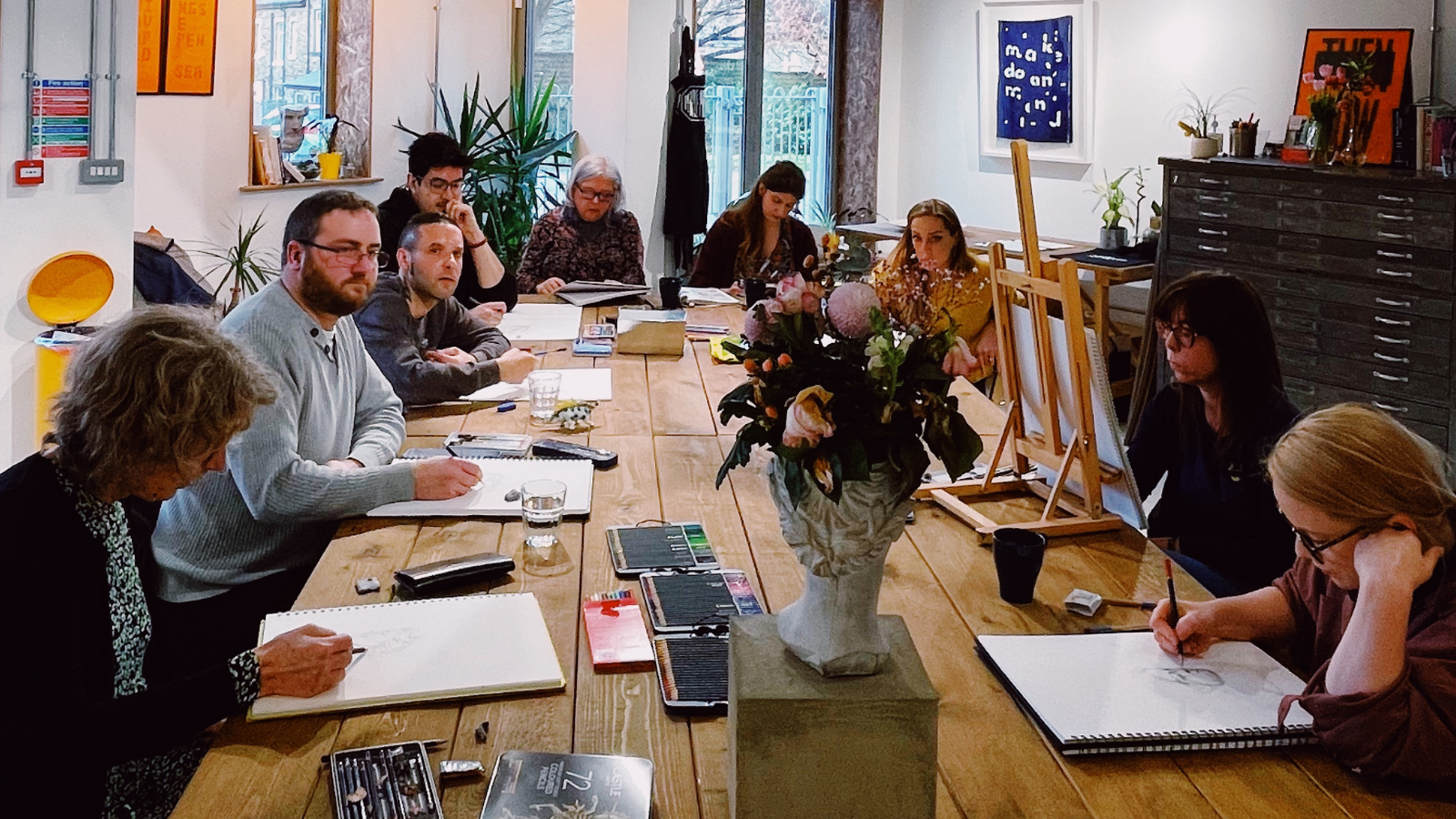 A photo from a Saltaire Art School drawing class with students around a table with sketch books
