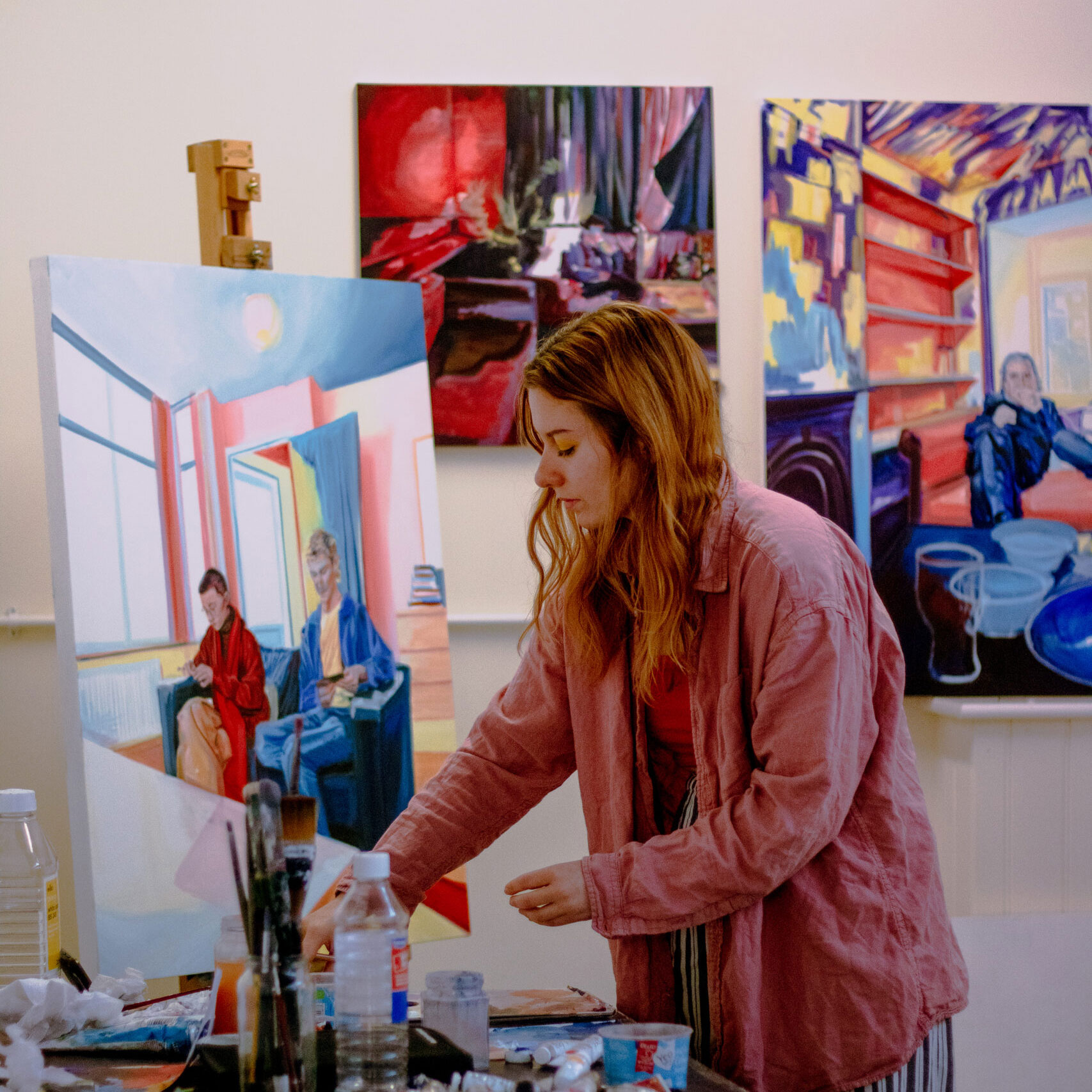 Artist Julia Pomeroy reaches for a paintbrush in her studio with brightly coloured paintings behind her