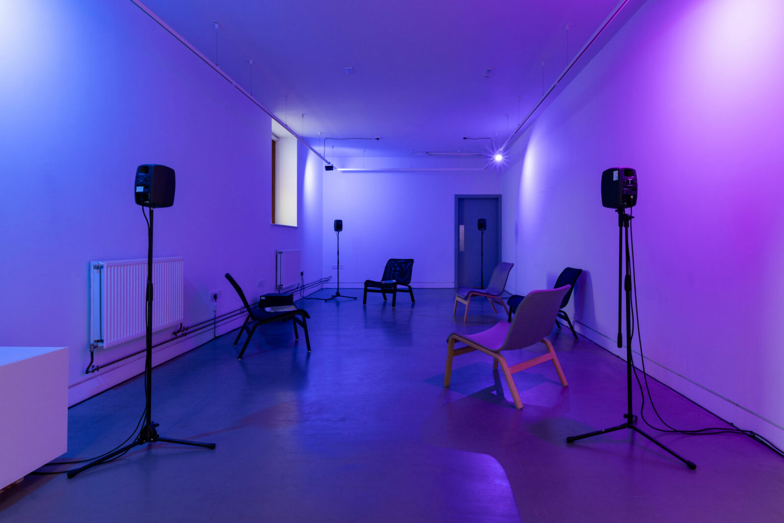 A purple lit gallery with chairs and speakers distributed across it
