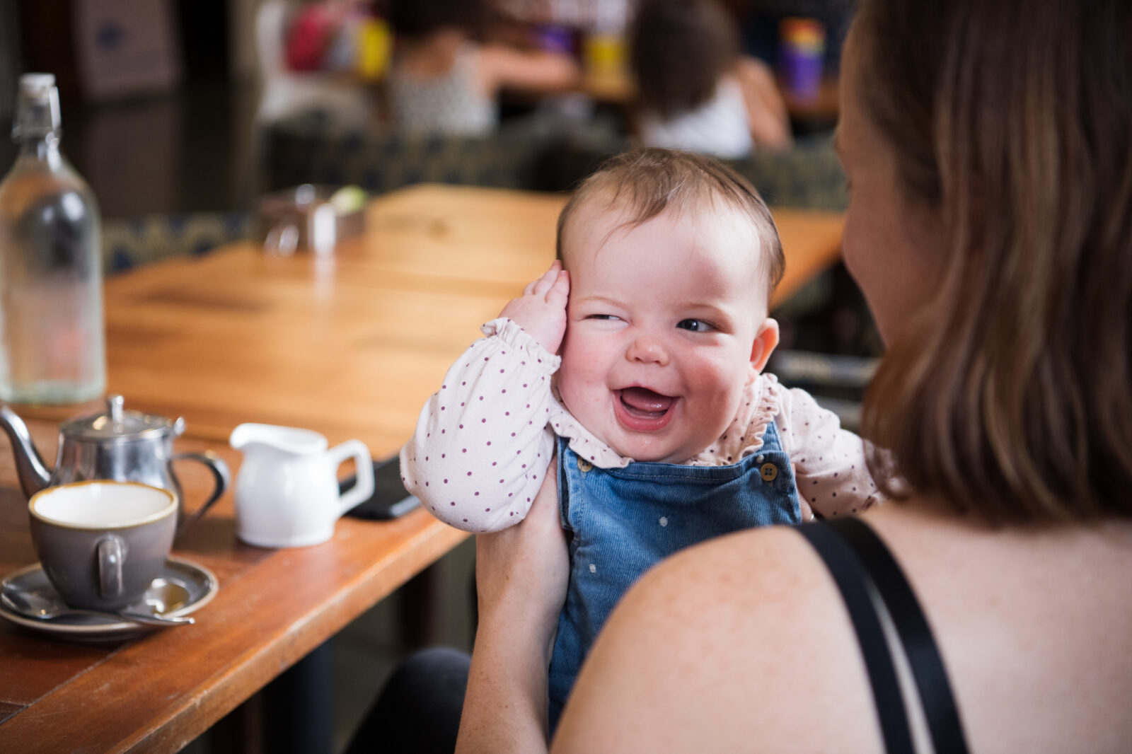 A smiling baby holds its hand to its head