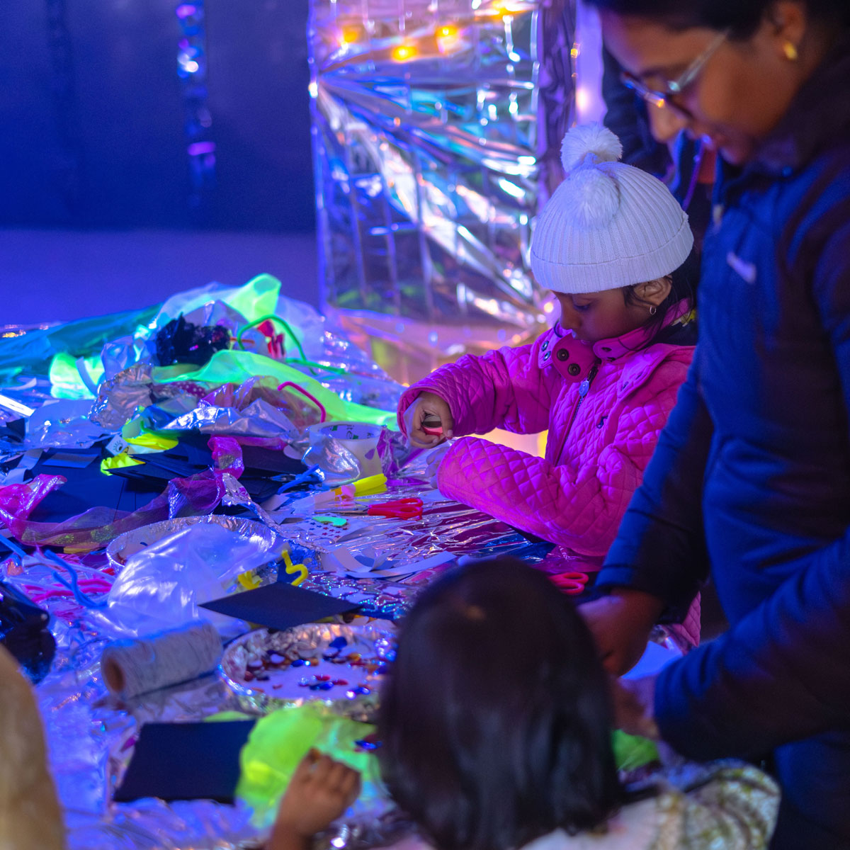 A family play in a neon lit space with sparkly materials